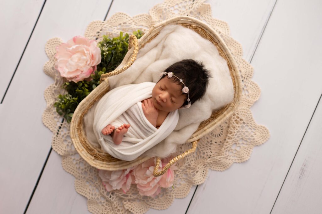 beautiful newborn baby girl session wrapped with toes peaking out, light florals and greenery, lying in a moses basket. 
