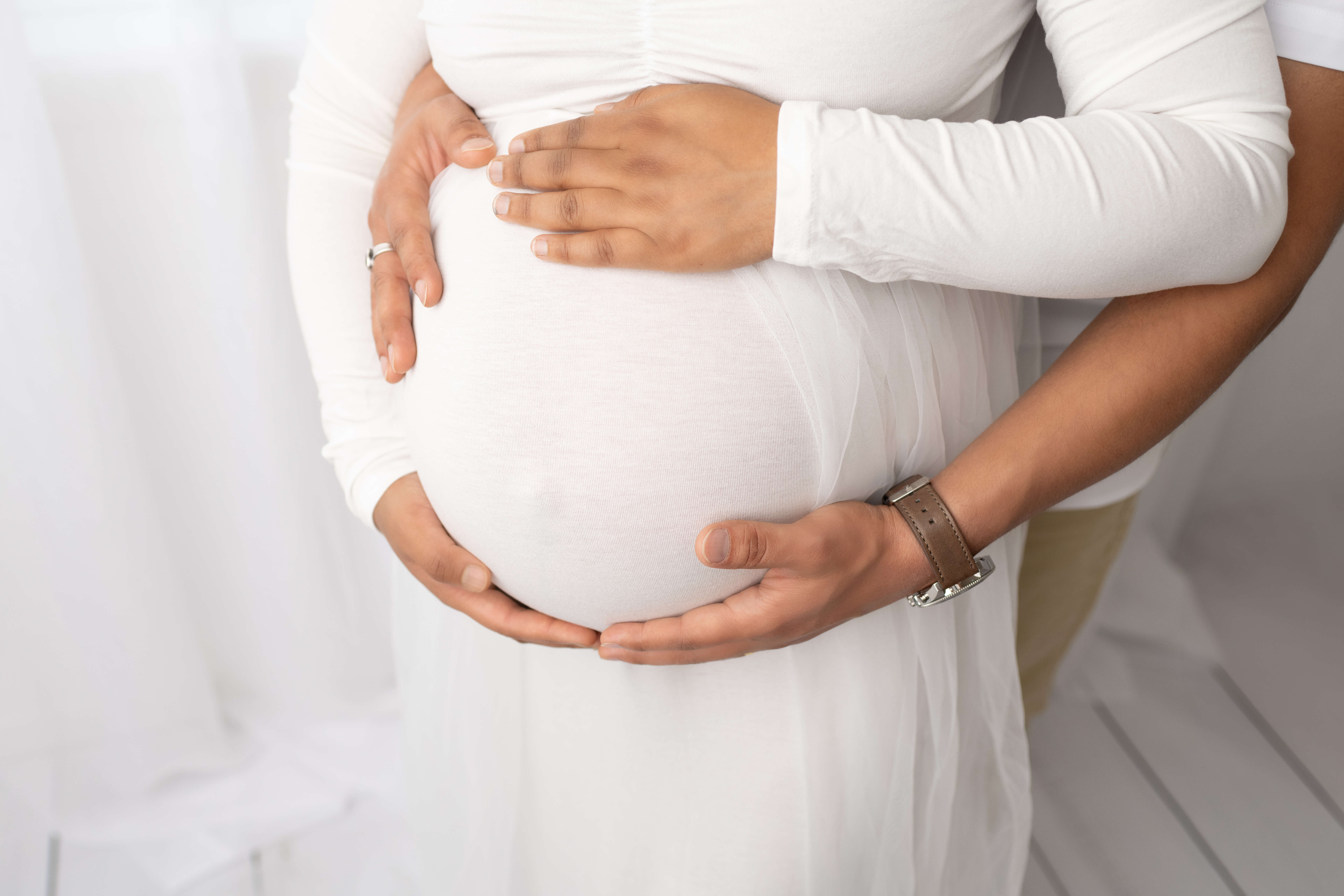 Details of mom and dad with hands on pregnancy bump while standing in a studio