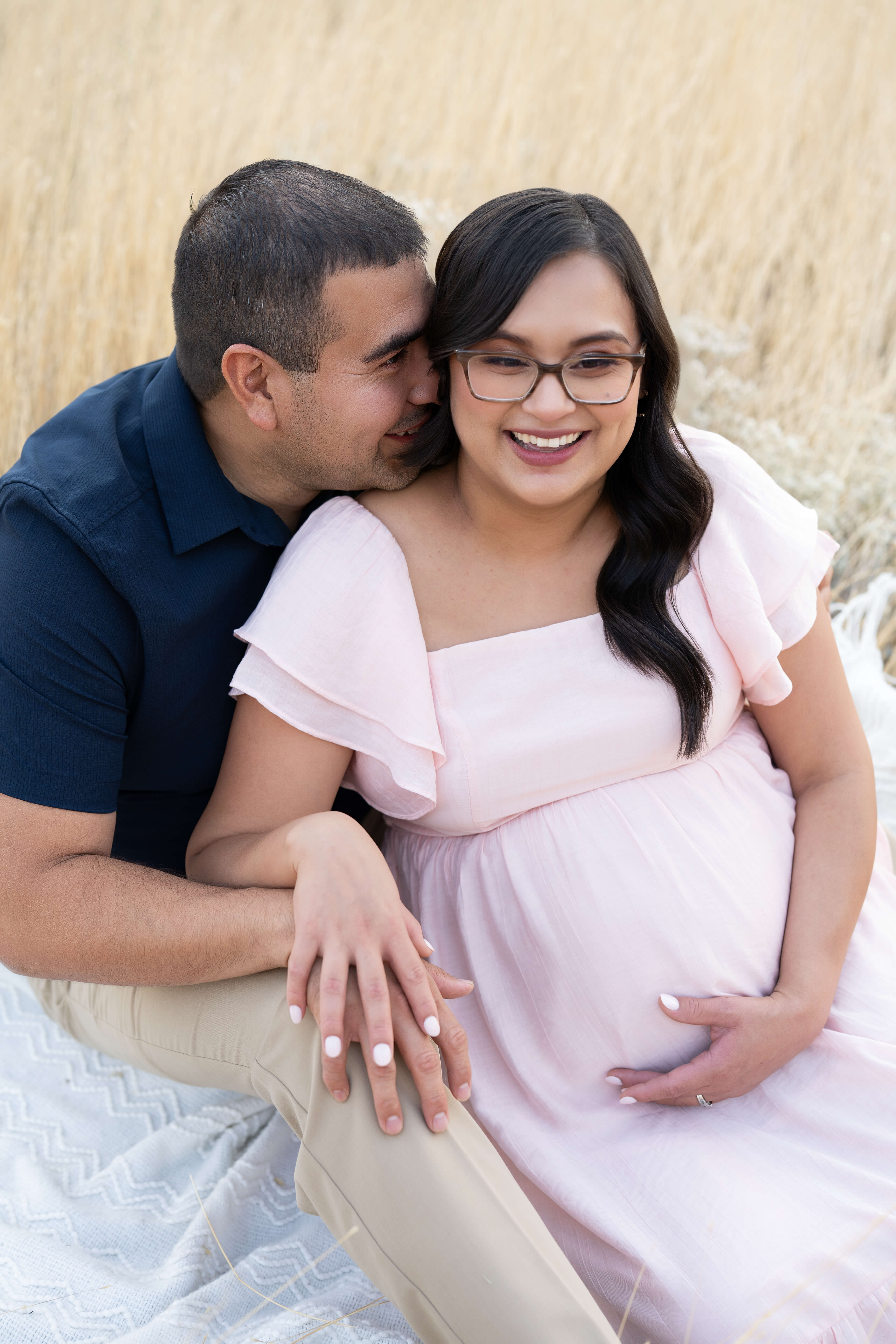 A happy expecting couple laugh while snuggling on a picnic blanket