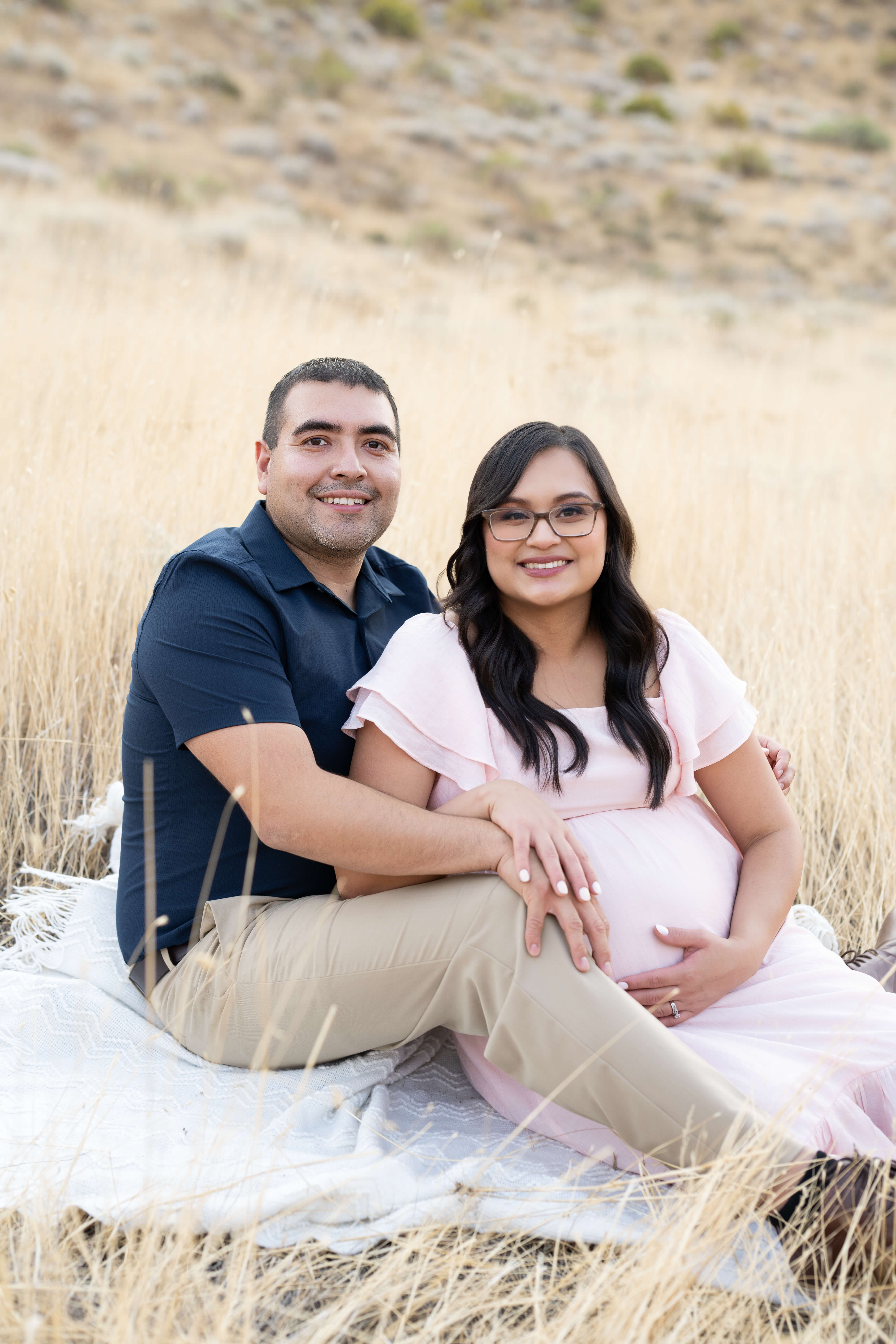A happy expecting couple snuggles on a hillside in pink and blue after visiting birth centers in tri cities wa