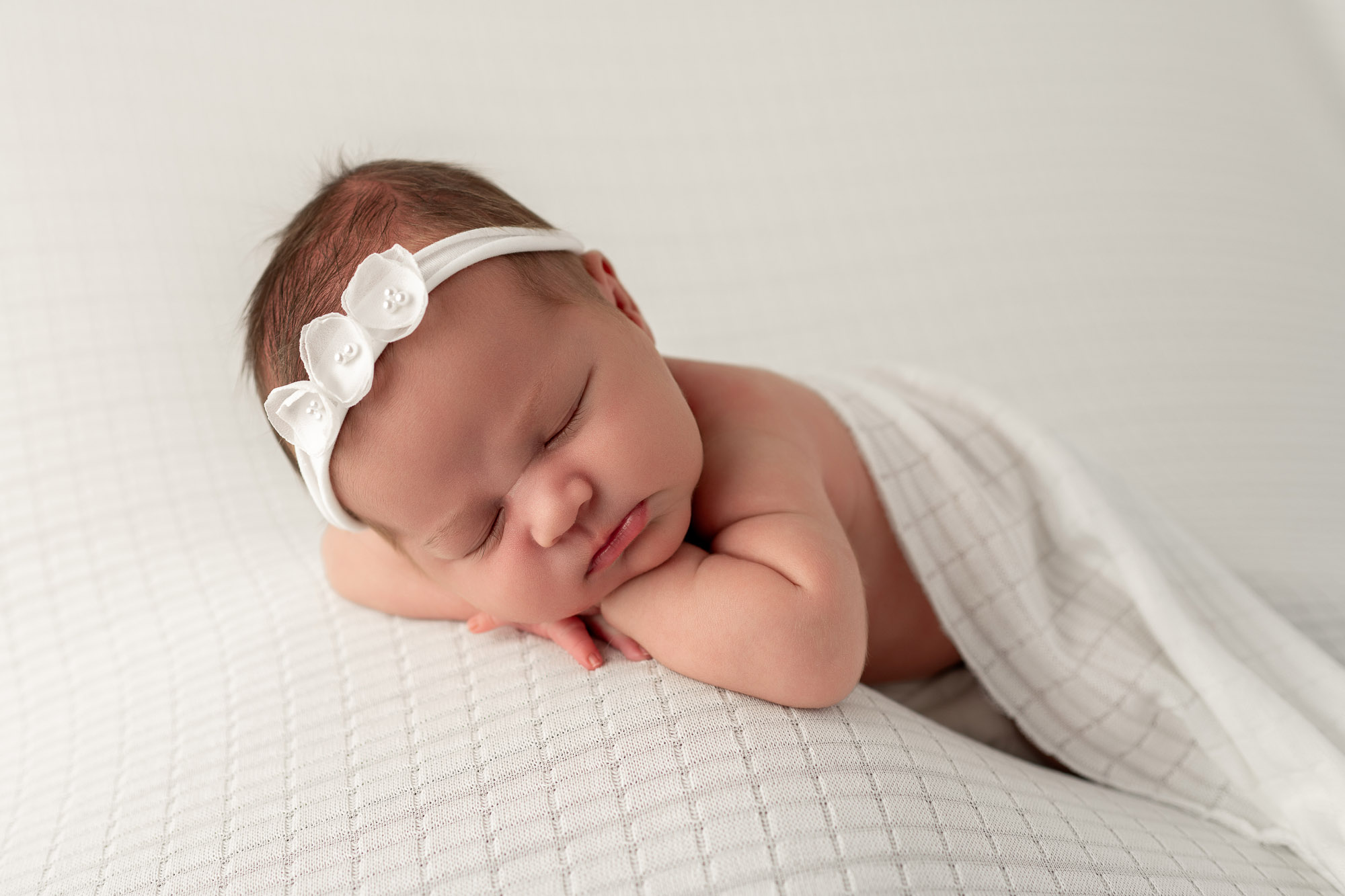 A sleeping newborn baby on her tummy rests on her hands in a white flower headband after meeting postpartum doulas in Tri-Cities, WA