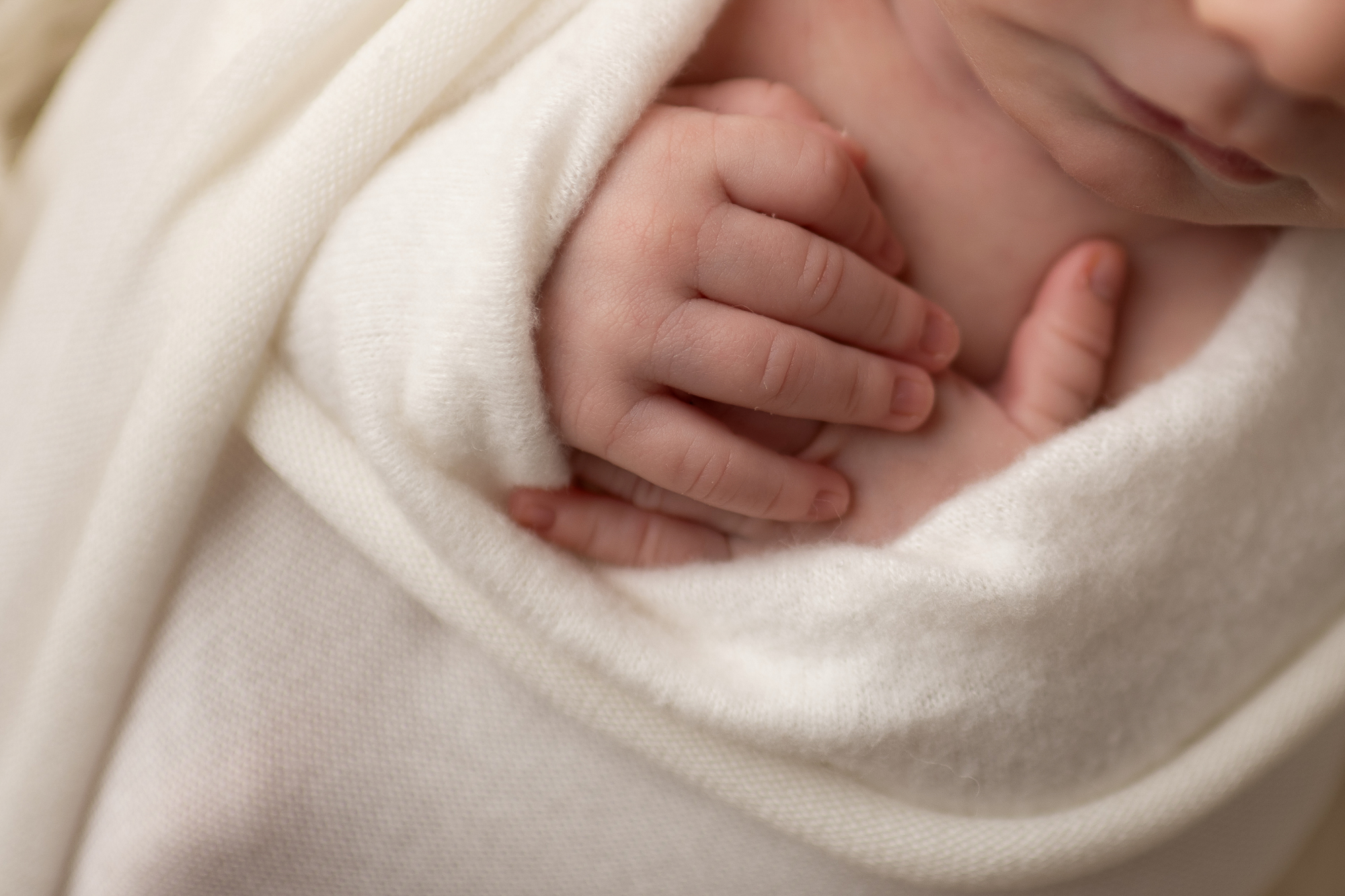 Details of a newborn baby's hands on its chest in a white swaddle