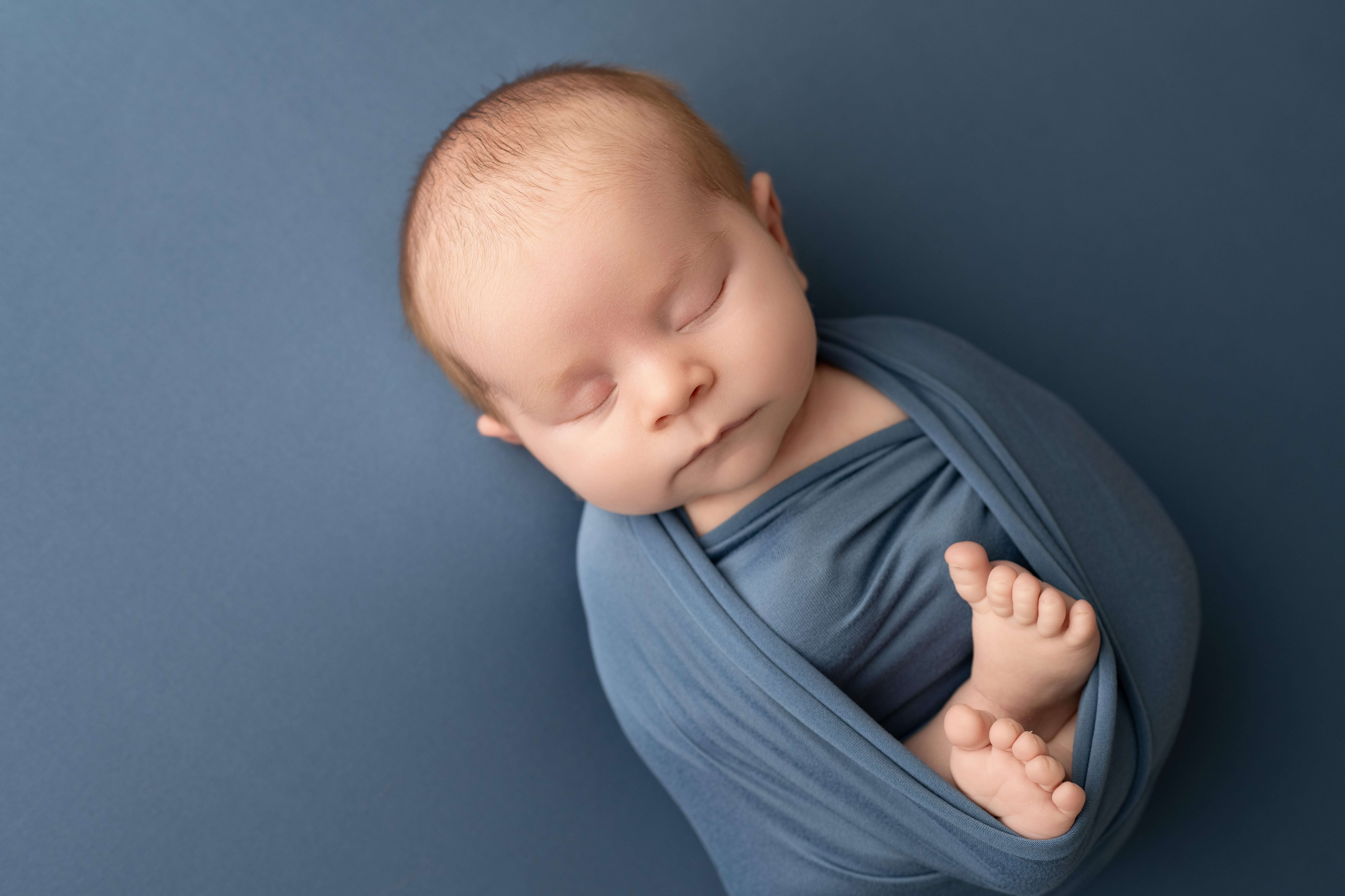 A sleeping newborn baby in blue swaddle with toes sticking out