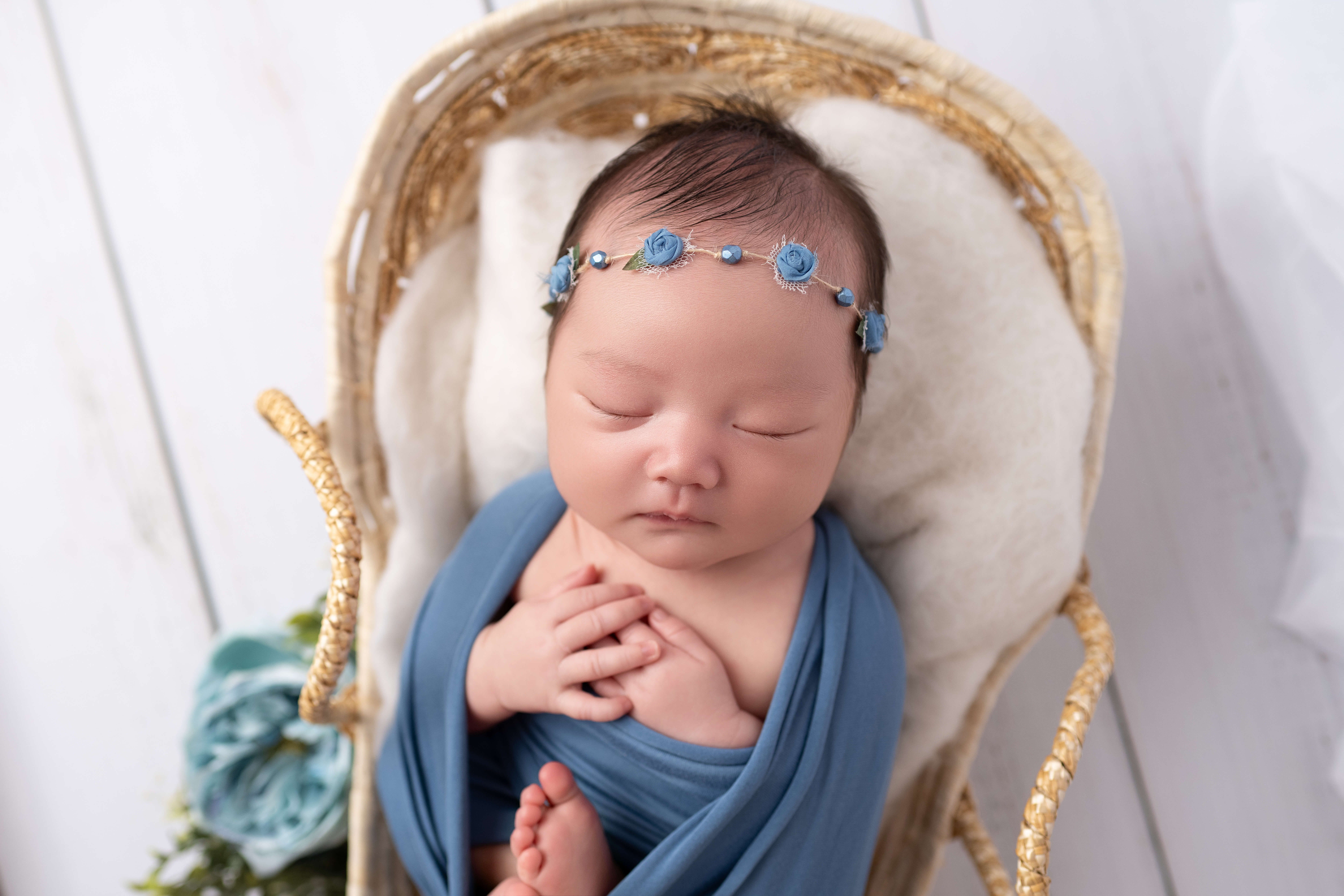 A newborn baby girl in a blue open swaddle in woven basket and flower headband after meeting lactation consultants in tri-cities